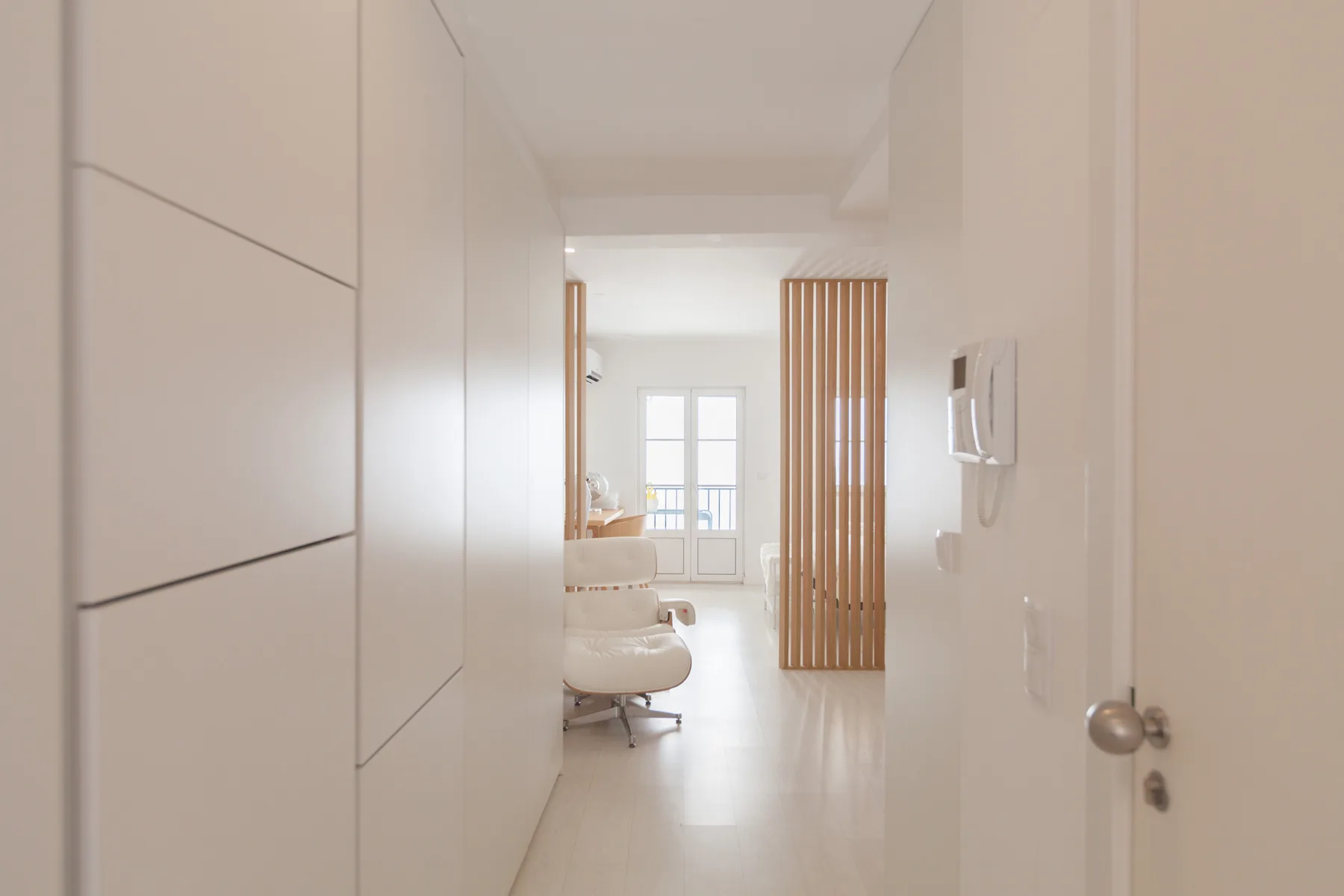 Un interior luminoso se abre hacia una sala de estar con una ventana y listones de madera.