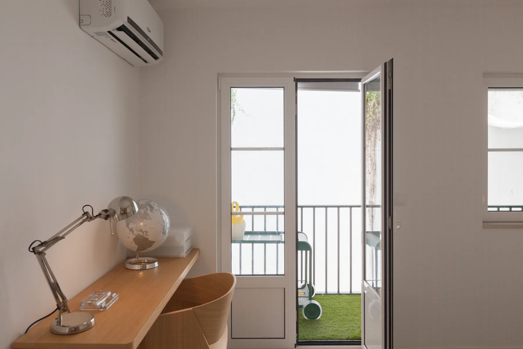 Una habitación luminosa con un escritorio junto a una puerta abierta al balcón.