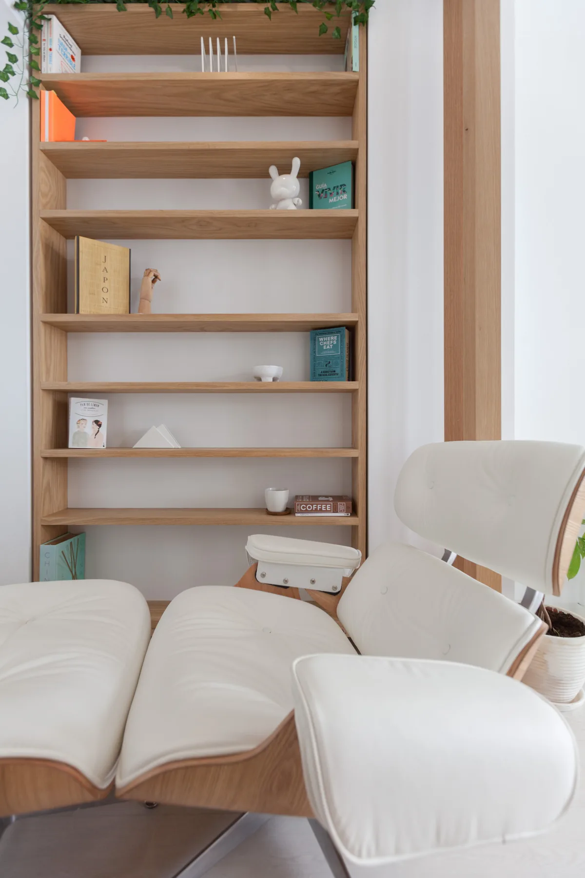 Un rincón de lectura luminoso con una estantería de madera y asientos blancos.