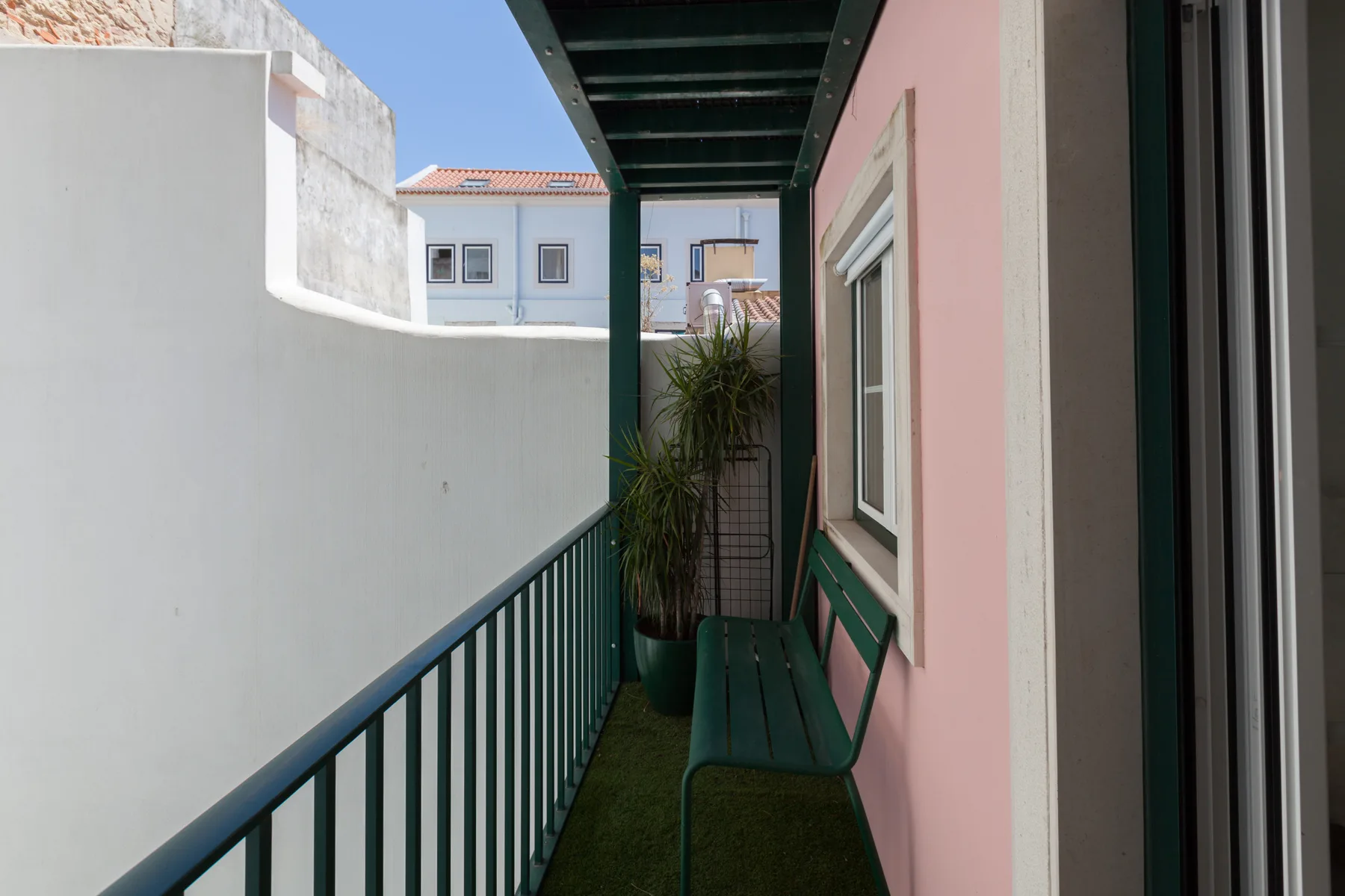 Un balcón exterior estrecho con barandilla verde, banco y una planta en maceta.