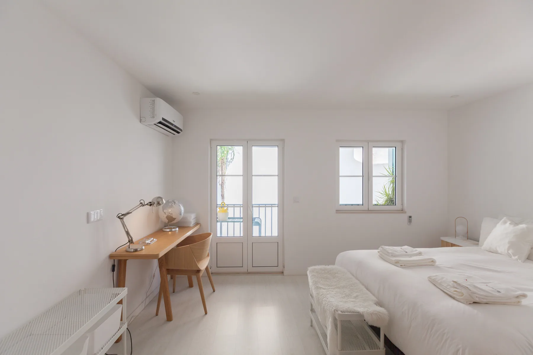 Un dormitorio luminoso con un escritorio junto a las ventanas y una cama bien tendida.
