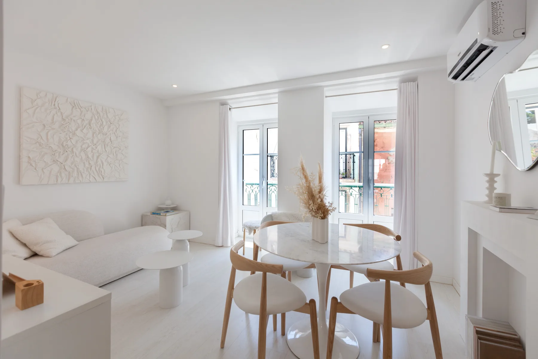 Una luminosa sala de estar y comedor con asientos, una mesa redonda y ventanas altas.