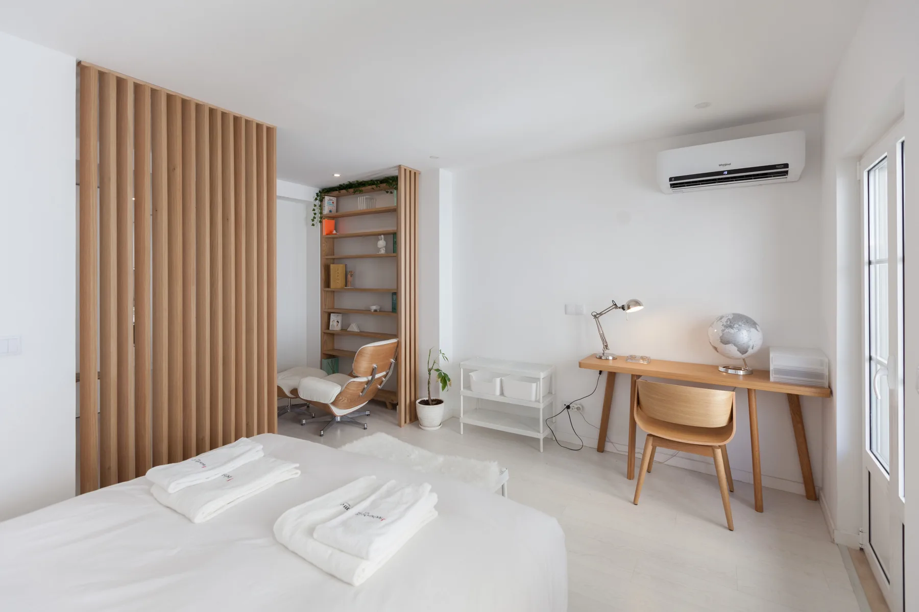 Un dormitorio luminoso con escritorio, estantería y un separador de listones de madera.
