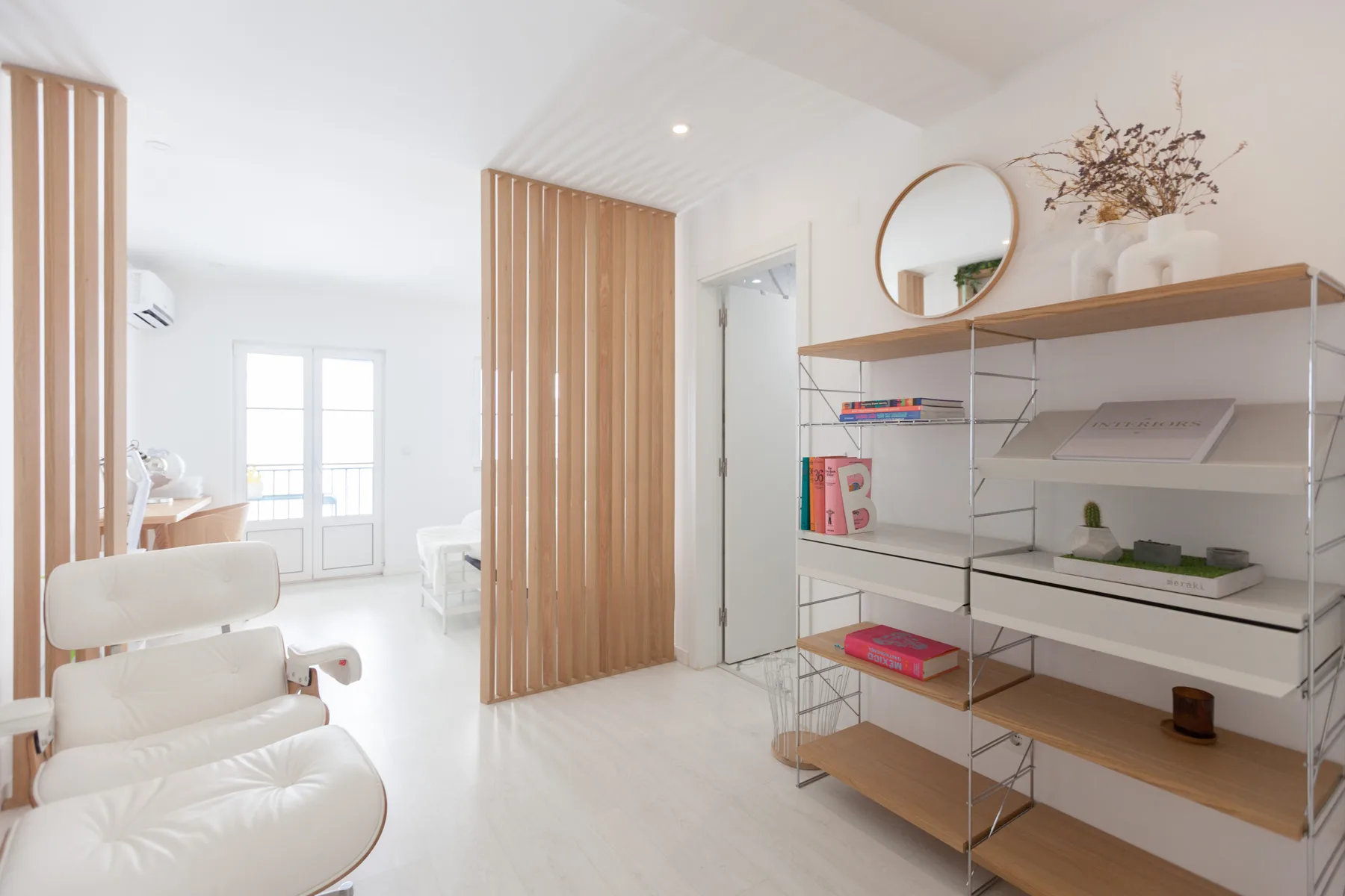 Una sala luminosa con asientos blancos, un separador de madera y estanterías abiertas.
