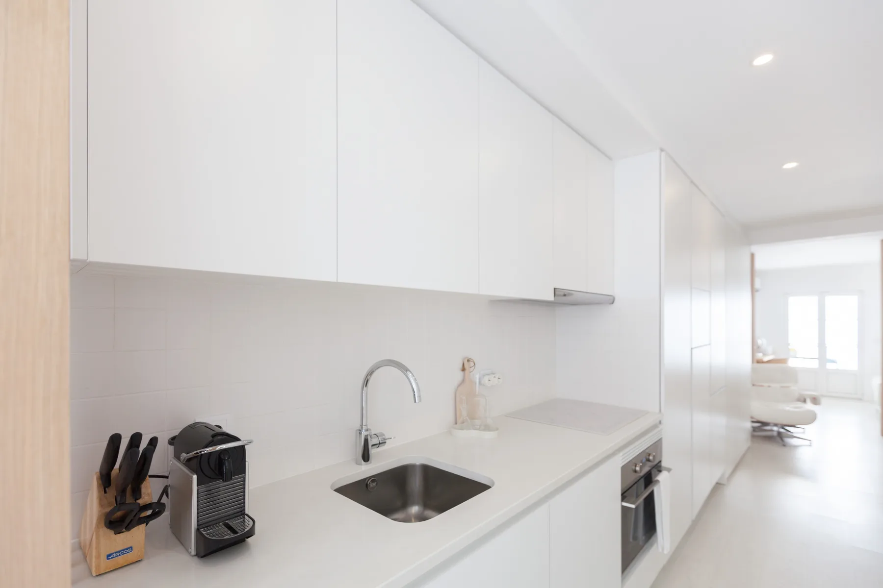 Una cocina blanca y luminosa con fregadero y encimera se abre a un comedor.
