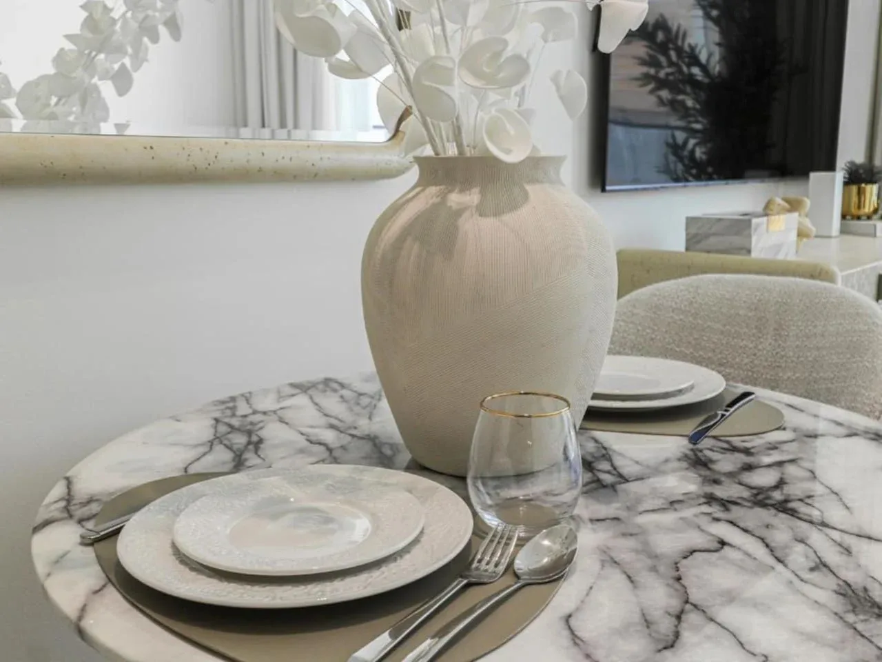 A dining table is set with plates and glassware beside a vase of flowers.