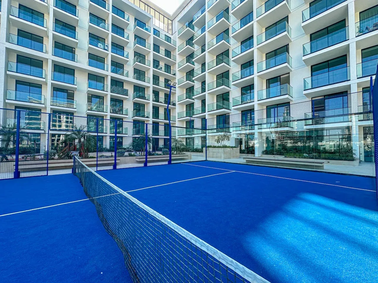 A blue court with a net sits in a courtyard surrounded by apartment buildings.