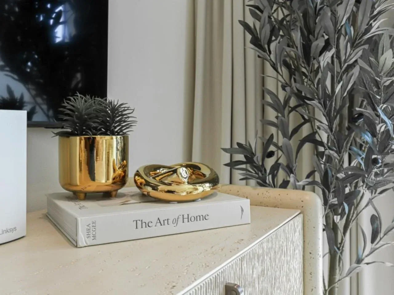 A living room console displays a book, a gold decorative bowl, and a potted plant.