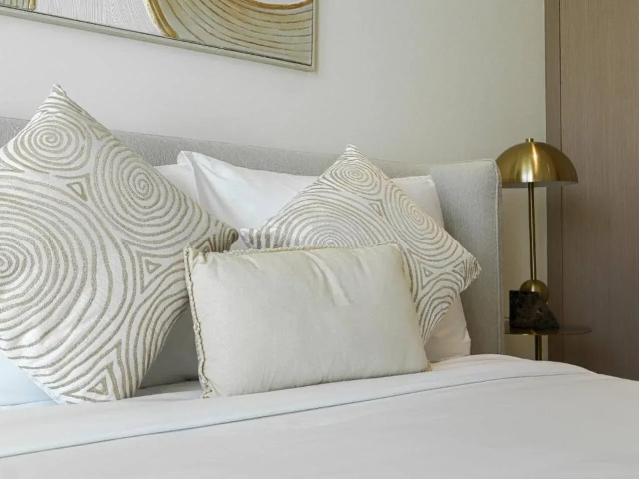 A neatly made bed with patterned cushions and a brass bedside lamp.