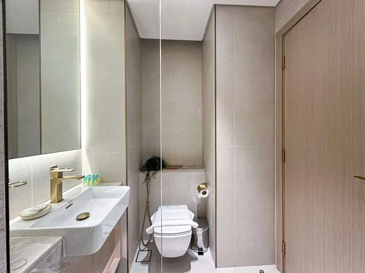 A bathroom with a wall-mounted sink, large mirror, and toilet.