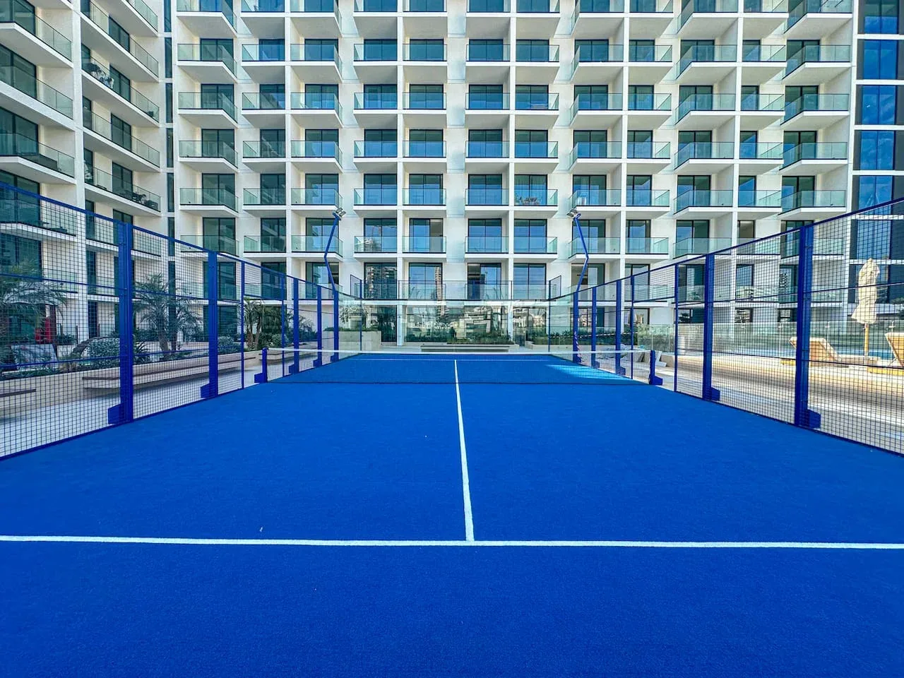 A blue sports court sits in front of a modern building with rows of balconies.