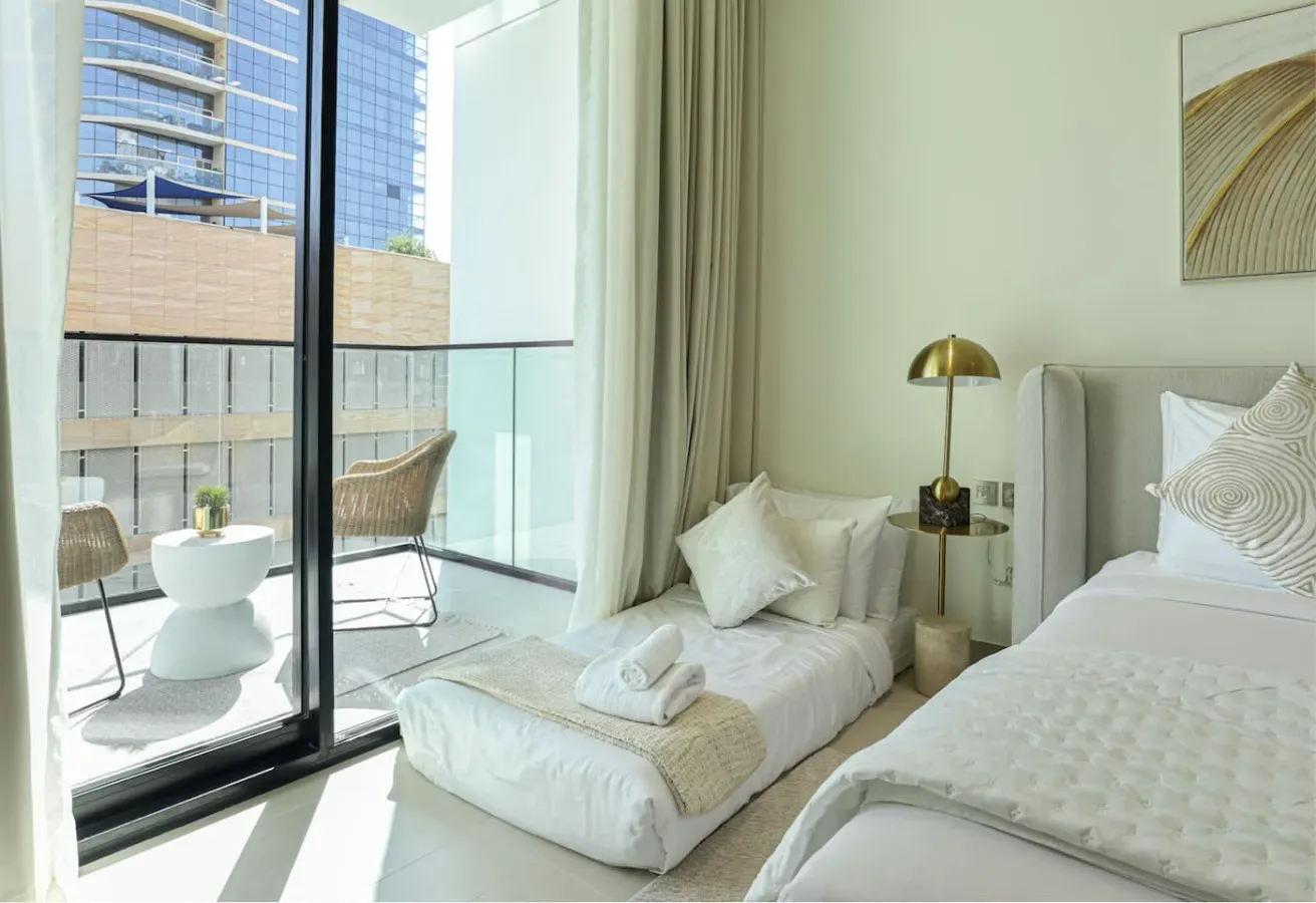 A bright bedroom with two beds beside a floor-to-ceiling window.