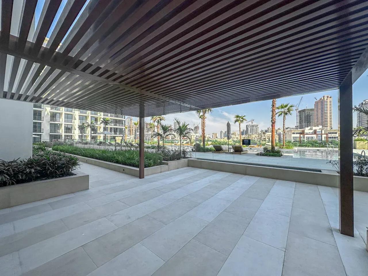 A covered outdoor terrace with a slatted overhead canopy and surrounding planters.