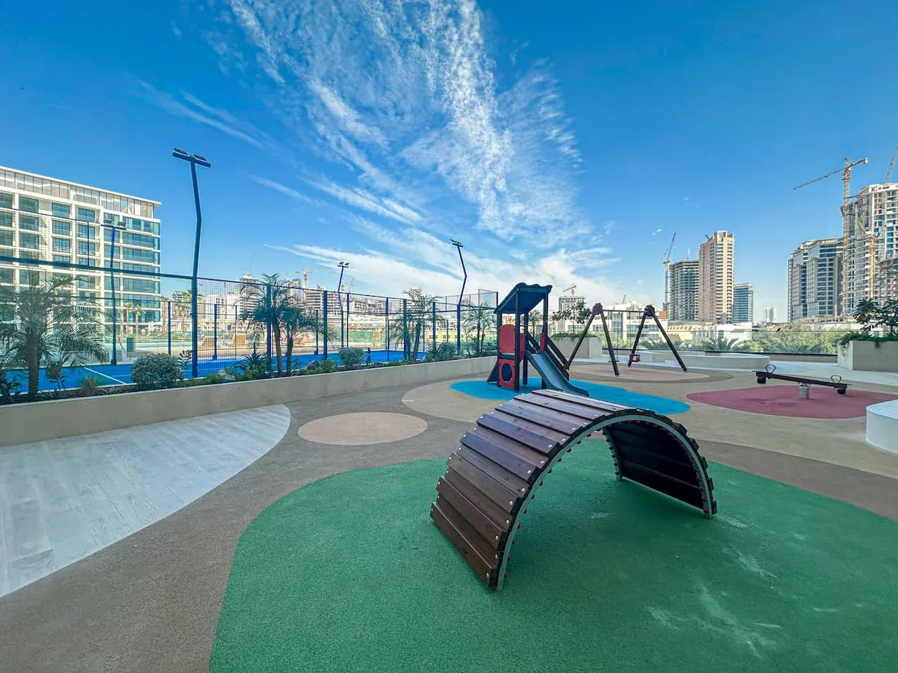 An outdoor playground with a curved climbing tunnel and play equipment.