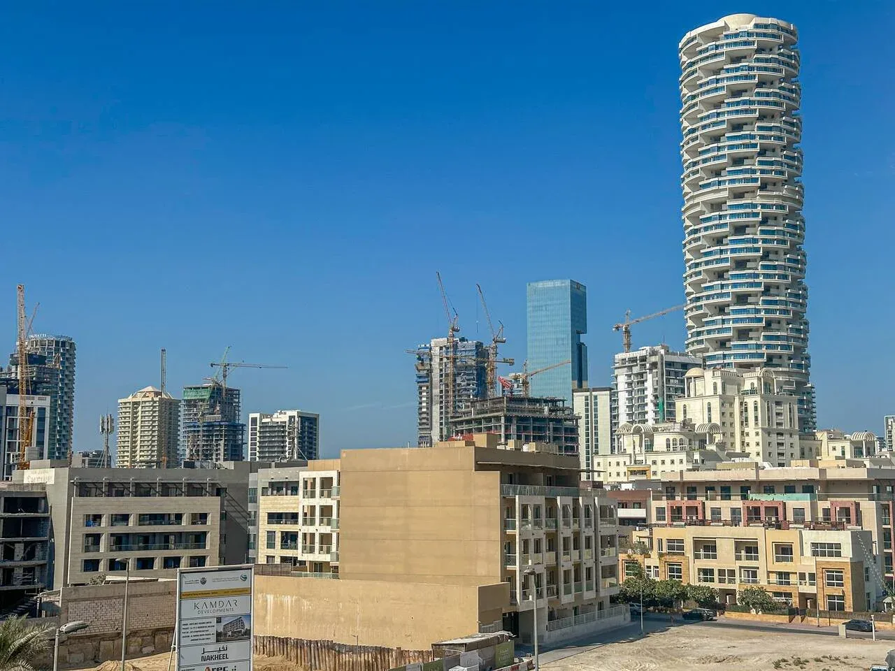 A city skyline with modern high-rise buildings and construction cranes under a clear sky.
