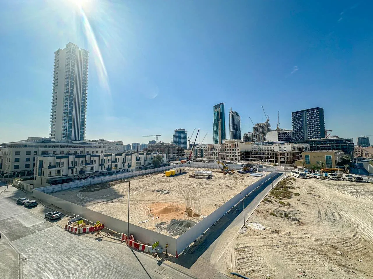 A construction site with a large cleared plot and high-rise buildings in the background.