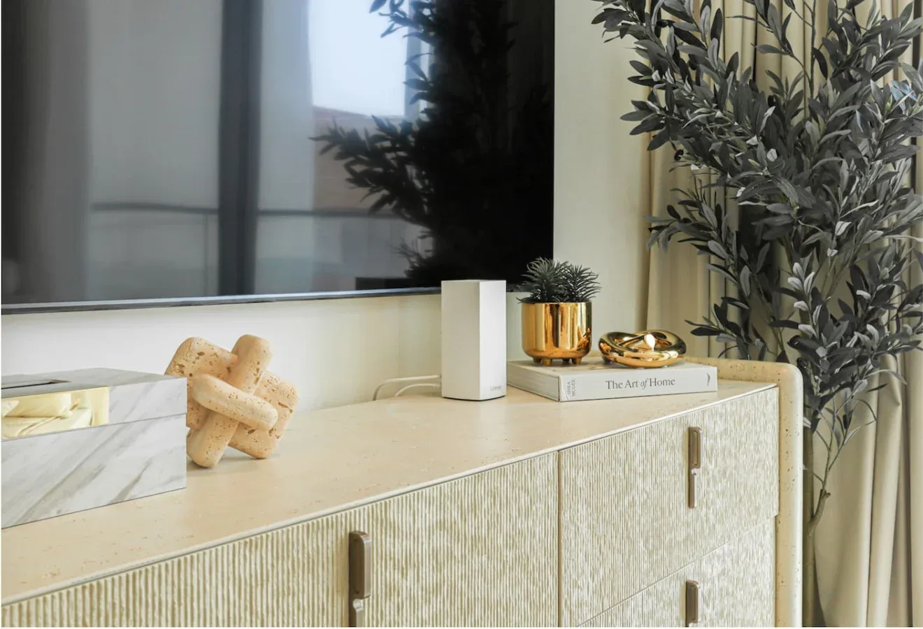 A light-colored sideboard sits beneath a window, with decorative plants and objects on top.