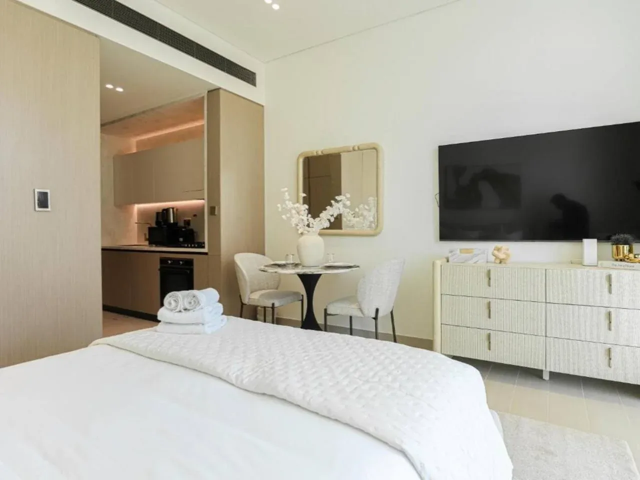 A bright bedroom with a neatly made bed, a small dining table, and a television.