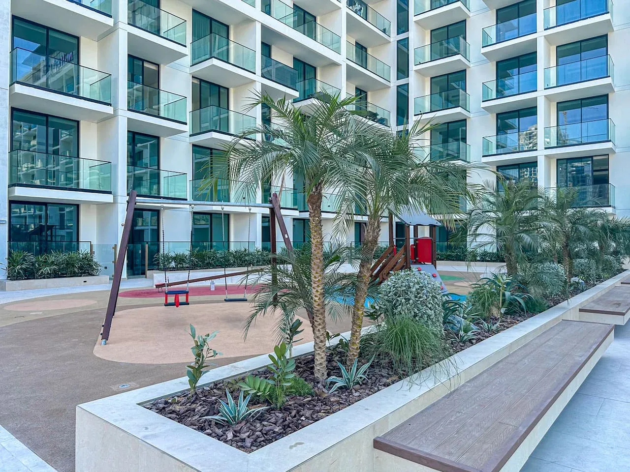 A landscaped courtyard with palm trees and seating beside a modern apartment building.