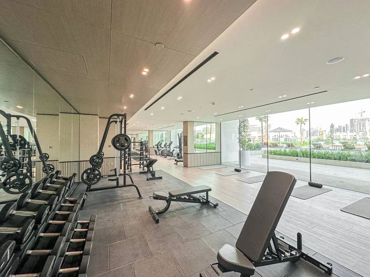 A bright fitness room with exercise equipment and large windows overlooking greenery.