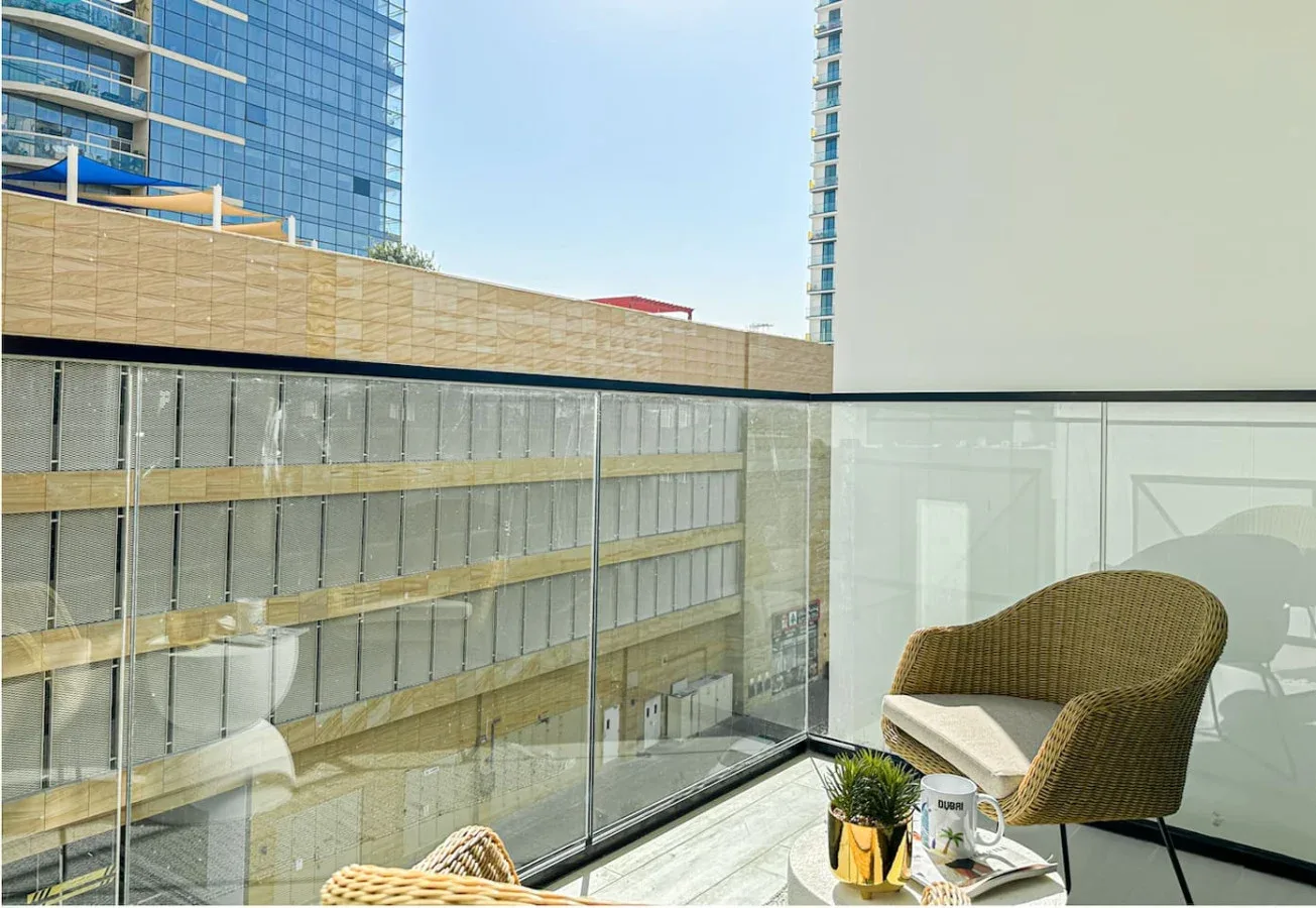 A glass balcony with woven seating overlooks a nearby modern building.