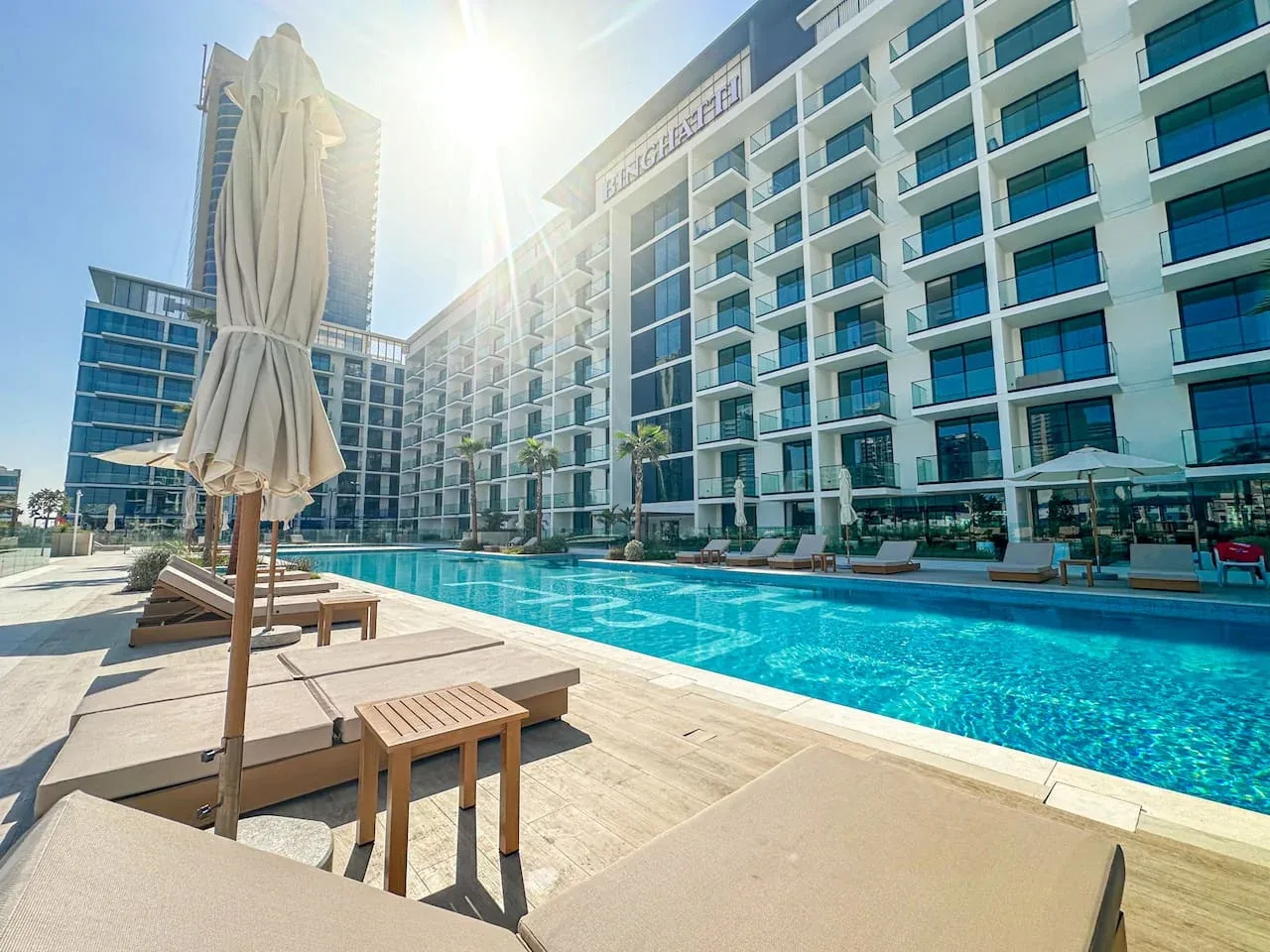 An outdoor pool beside a modern multi-story building, with loungers on the deck.