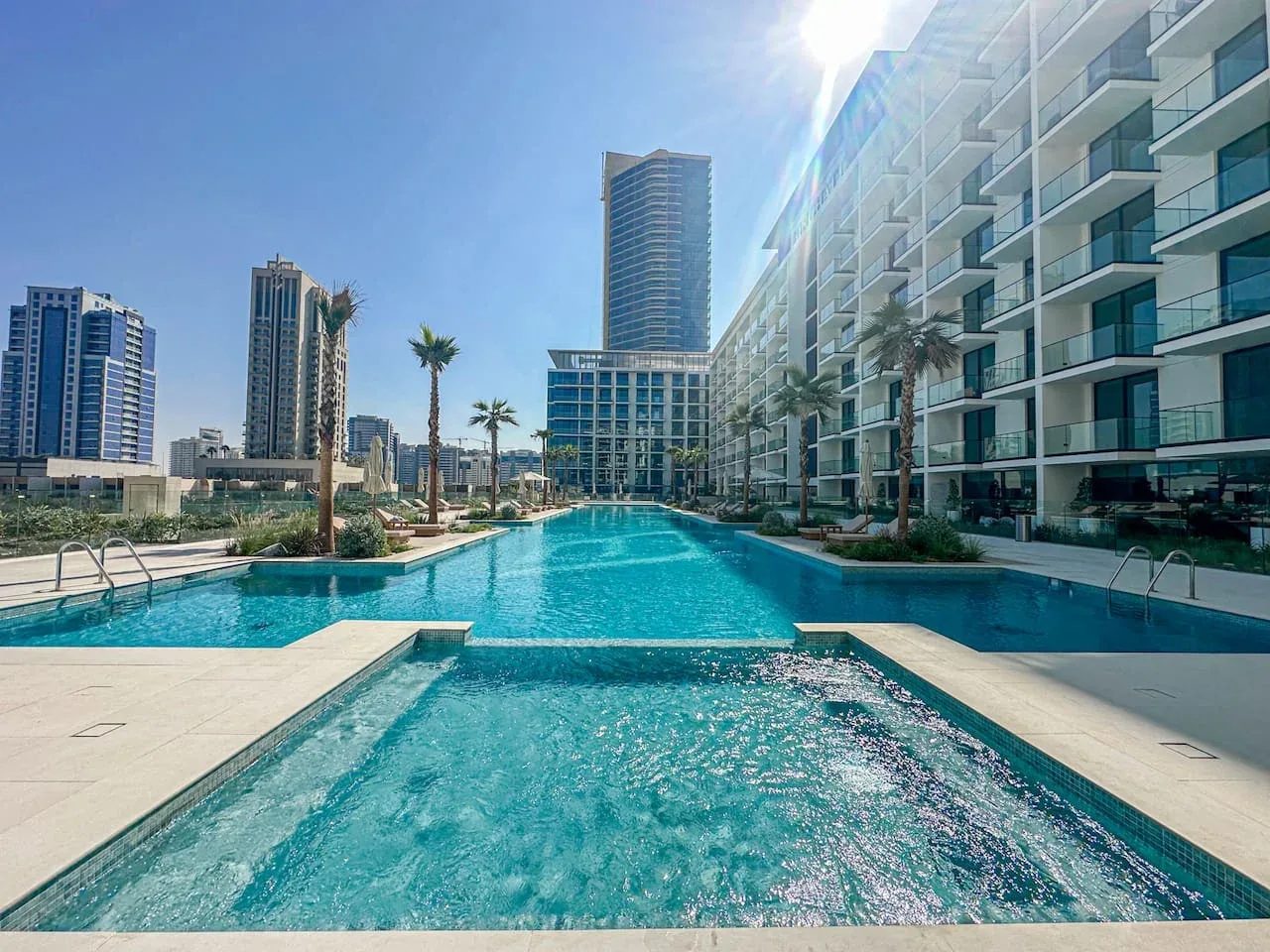 A swimming pool sits beside a modern high-rise building under a clear blue sky.