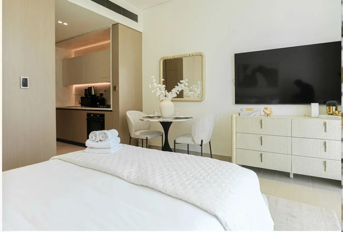 A bedroom with a neatly made bed, dining table, and wall-mounted television.