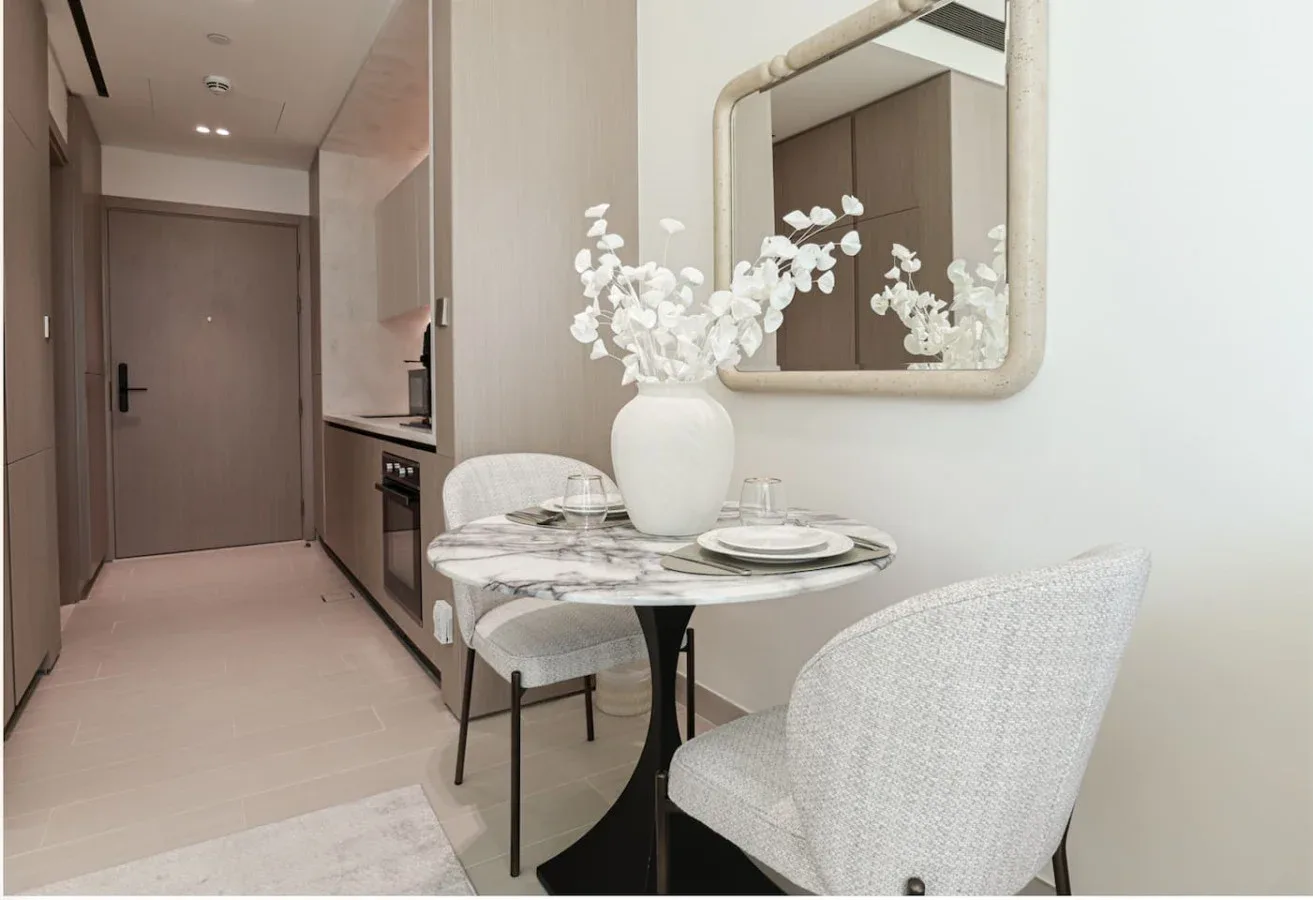 A dining nook with a round table, pale chairs, and flowers in a vase.
