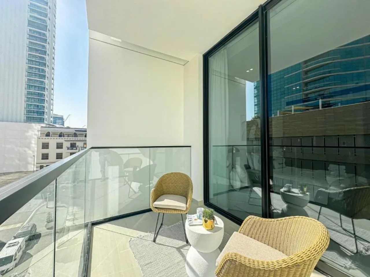 A balcony with wicker seating and a glass railing overlooks nearby buildings.