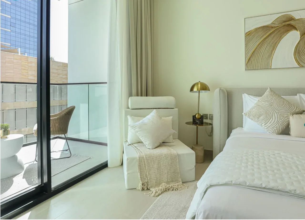 A bright bedroom with a bed, an armchair, and glass doors opening to a balcony.