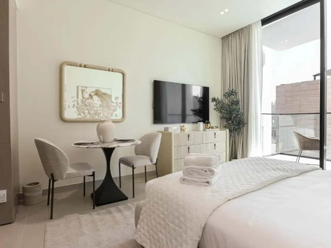 A bright bedroom with a neatly made bed, a television, and a small table.