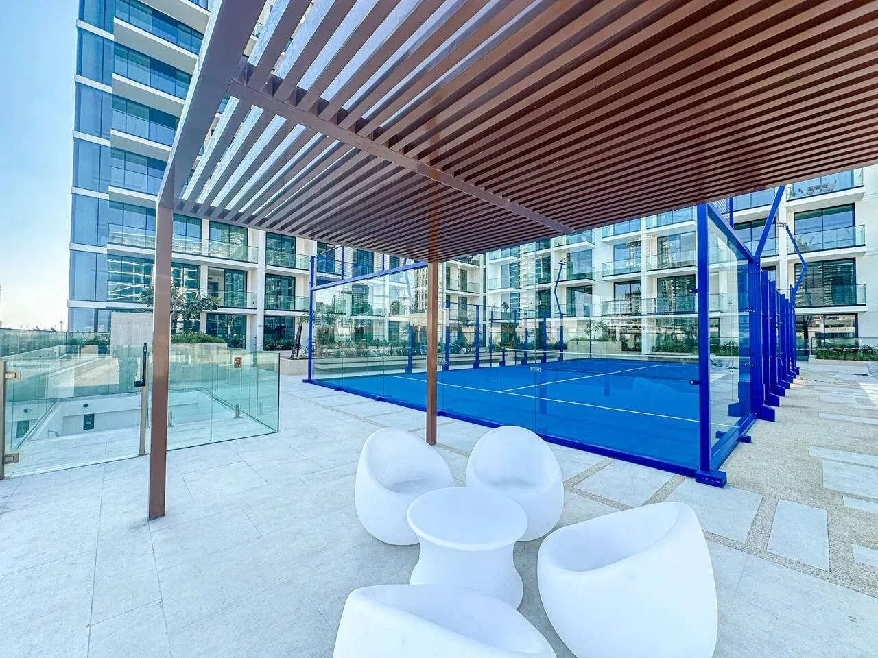 An outdoor court sits beside a glass-fronted building under a slatted canopy.