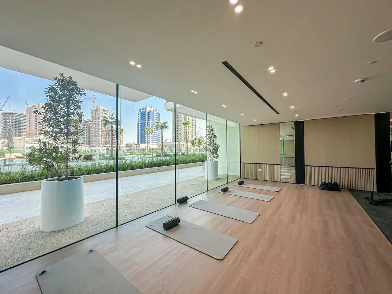 A bright exercise room with mats arranged beside floor-to-ceiling windows.