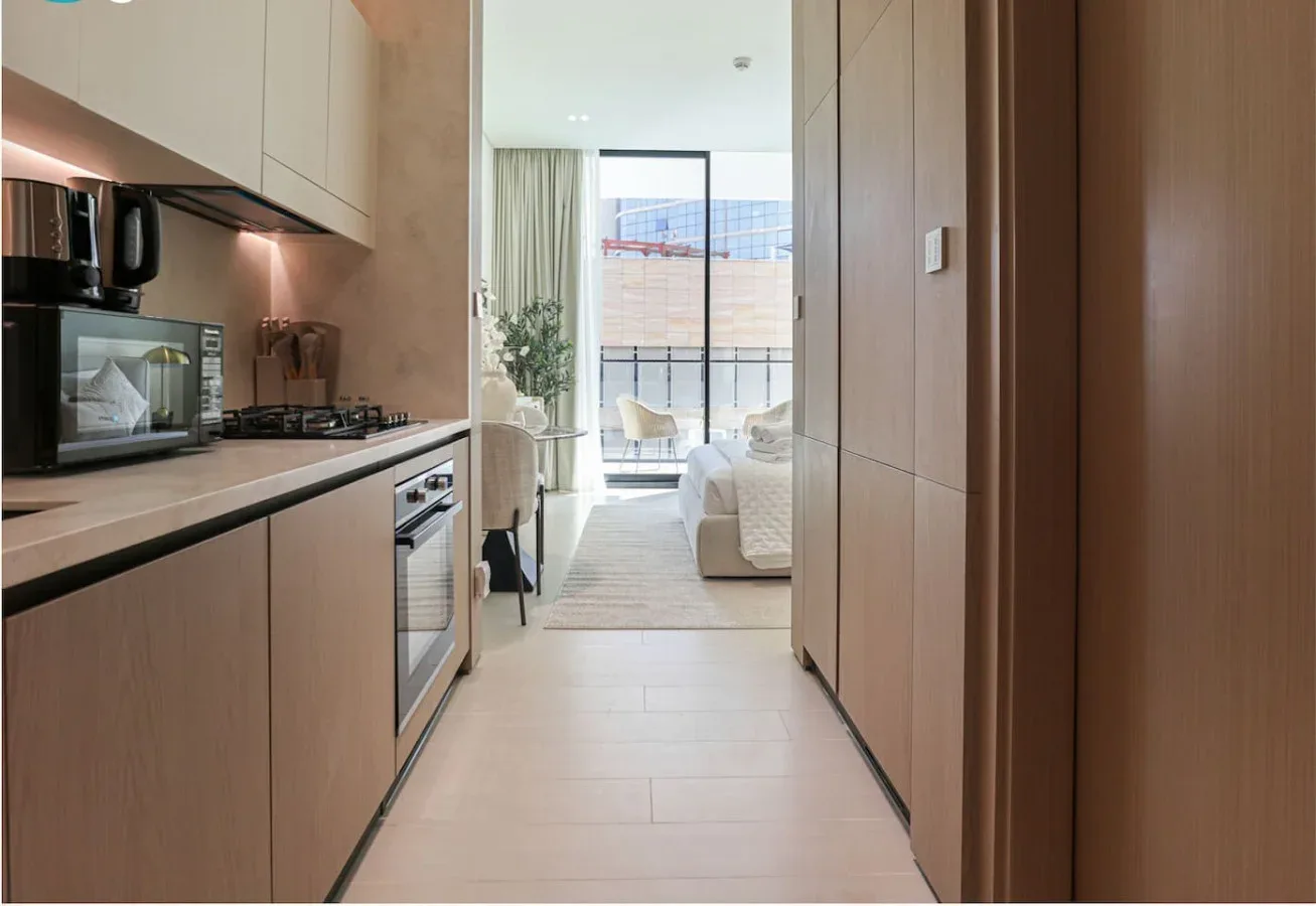 A narrow kitchen opens toward a bright living area with large windows.