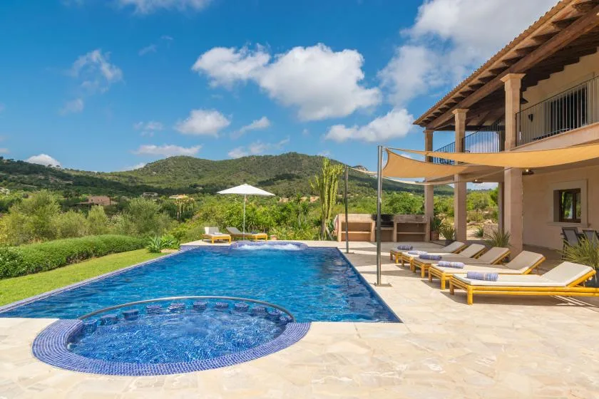 Una piscina exterior junto a un patio con asientos reclinables y una terraza sombreada.