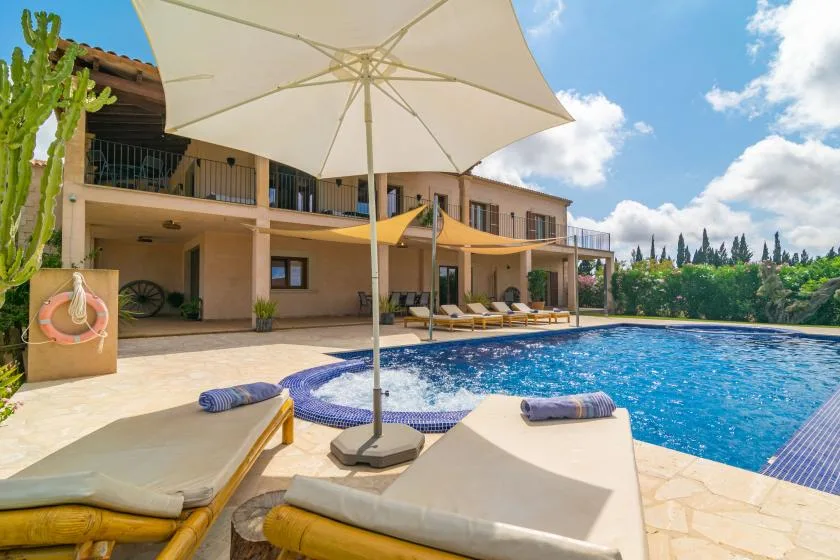 Un patio soleado junto a la piscina con tumbonas y una gran sombrilla.