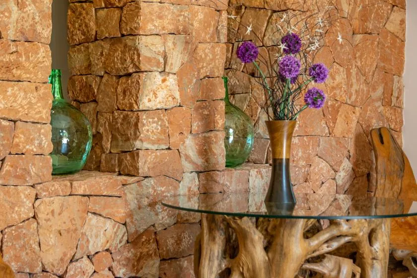 Un estante de vidrio con jarrones decorativos está junto a una pared de piedra rústica.