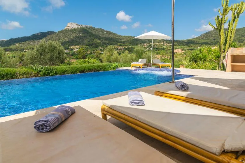 Una piscina al aire libre junto a tumbonas, con colinas verdes al fondo.