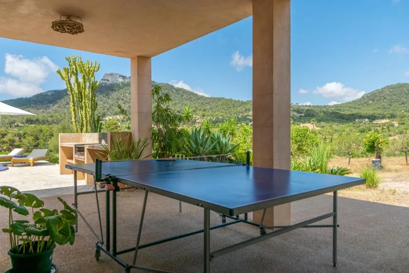 Un patio exterior cubierto con una mesa de ping-pong frente a colinas verdes.