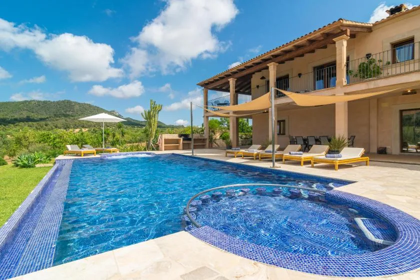 Una piscina con un spa circular junto a un patio con sombra.