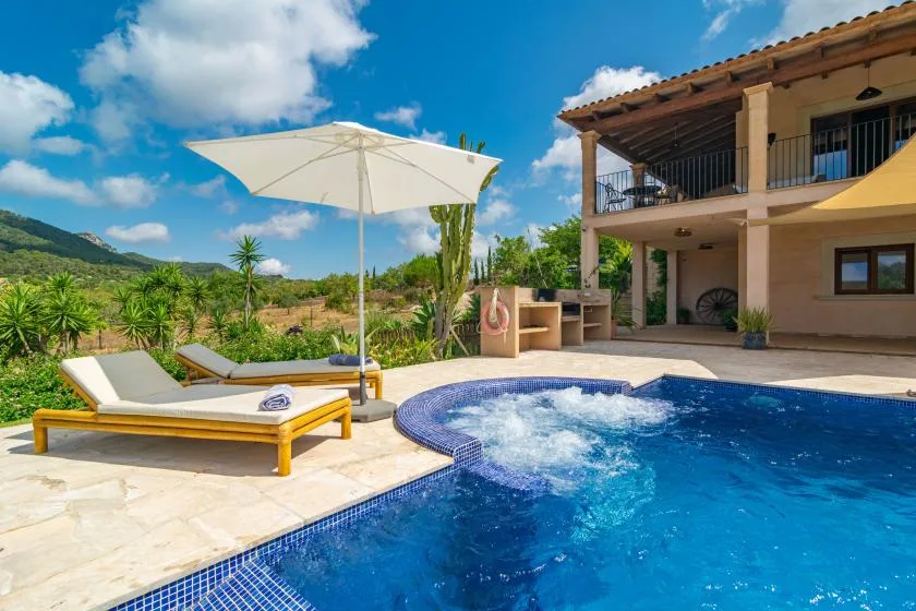 Una piscina al aire libre junto a una casa, con asientos y una sombrilla.