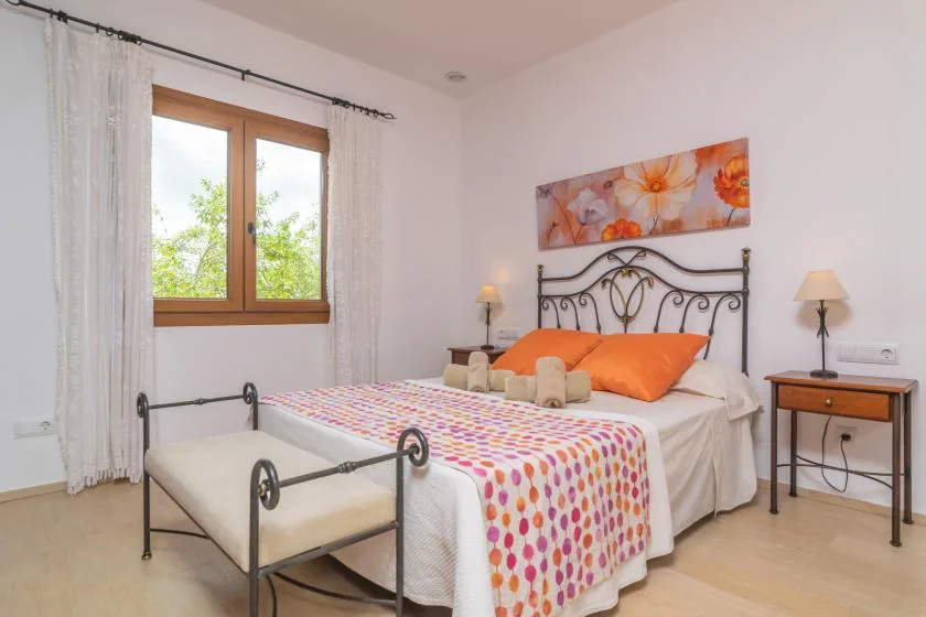 Un dormitorio con una cama de metal, ropa de cama colorida y una ventana con cortinas.