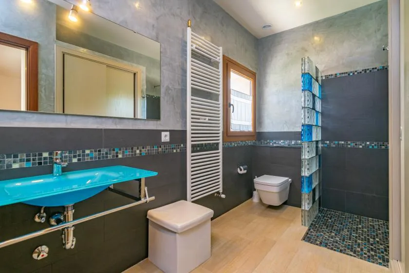 Un baño moderno con un lavabo turquesa y una zona de ducha con azulejos.
