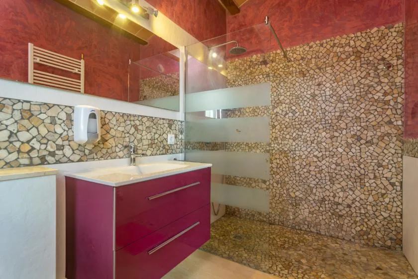 Un baño con lavabo y ducha de vidrio junto a una pared con diseño de piedra.