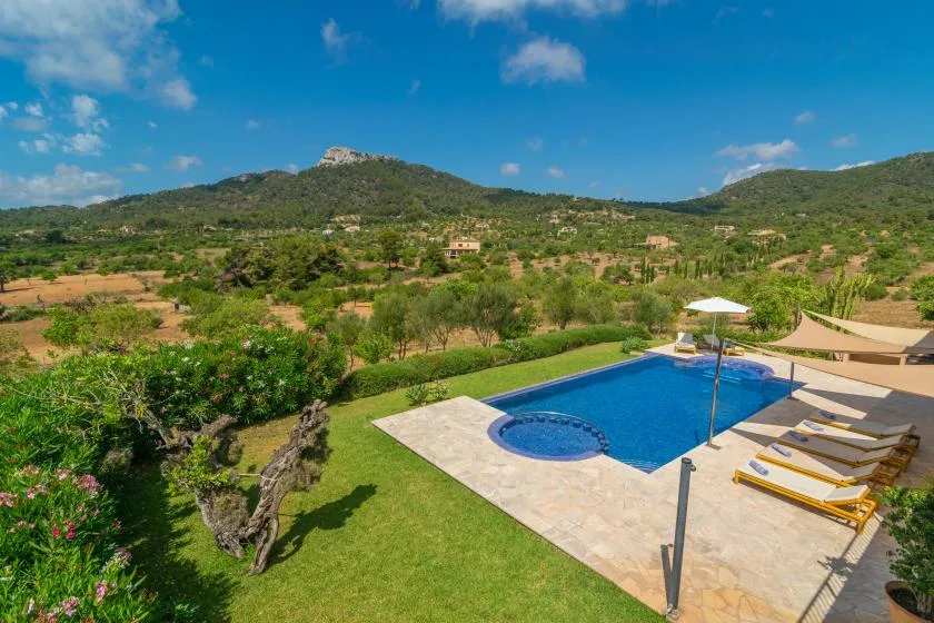 Una piscina al aire libre junto a un césped, con colinas verdes al fondo.