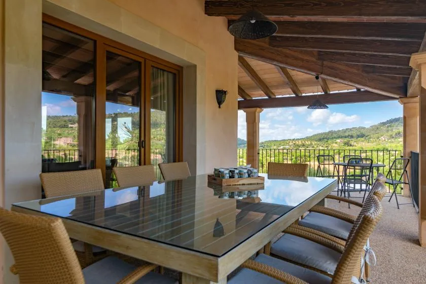 Comedor exterior cubierto con una mesa de vidrio y vistas a colinas verdes.