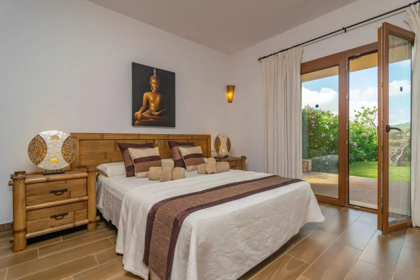 Un dormitorio con una cama, mesitas de noche y puertas de vidrio que dan a un jardín.