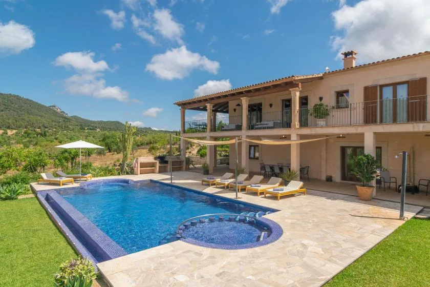 Una piscina está junto a una casa grande, con colinas verdes a lo lejos.