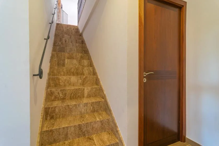 Una escalera de azulejos con pasamanos sube junto a una puerta de madera.